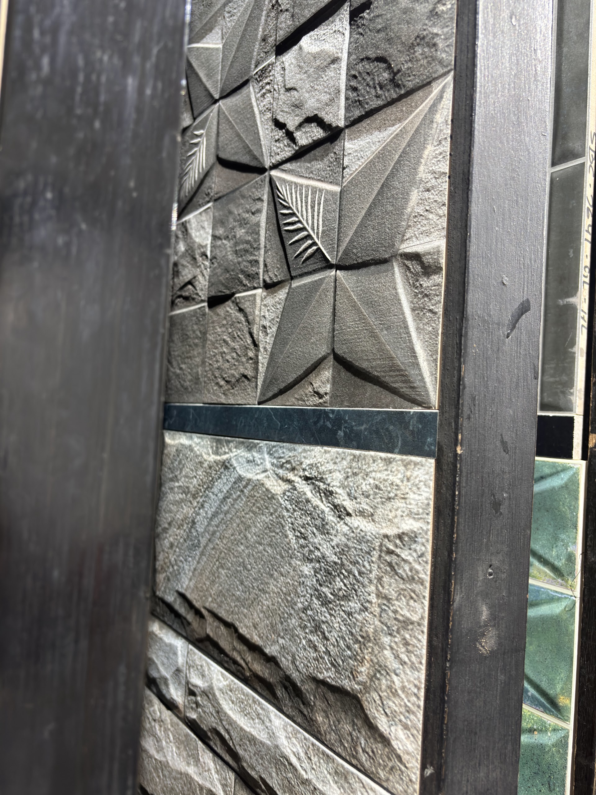 Grey 3D stone texture and faceted relief tile panels displayed in a showroom rack