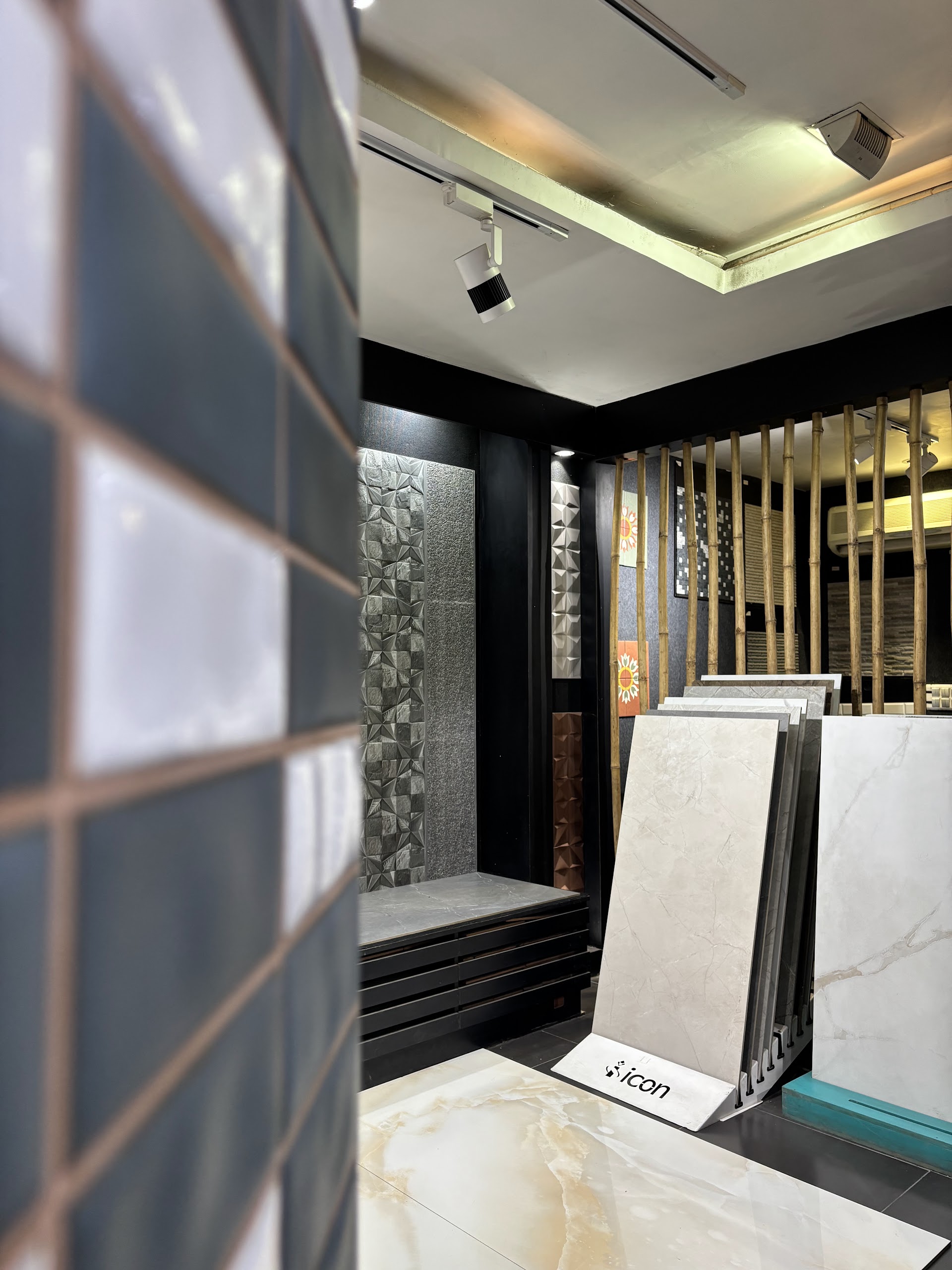 Close view along a grey tiled display with sample racks and directional ceiling lighting behind it