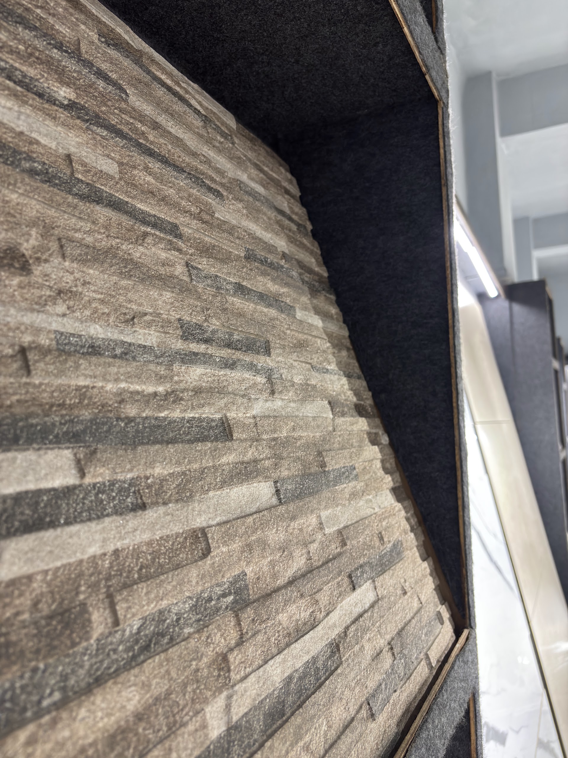 Angled close-up of a layered stone-finish tile display with horizontal ridges in warm grey and beige tones
