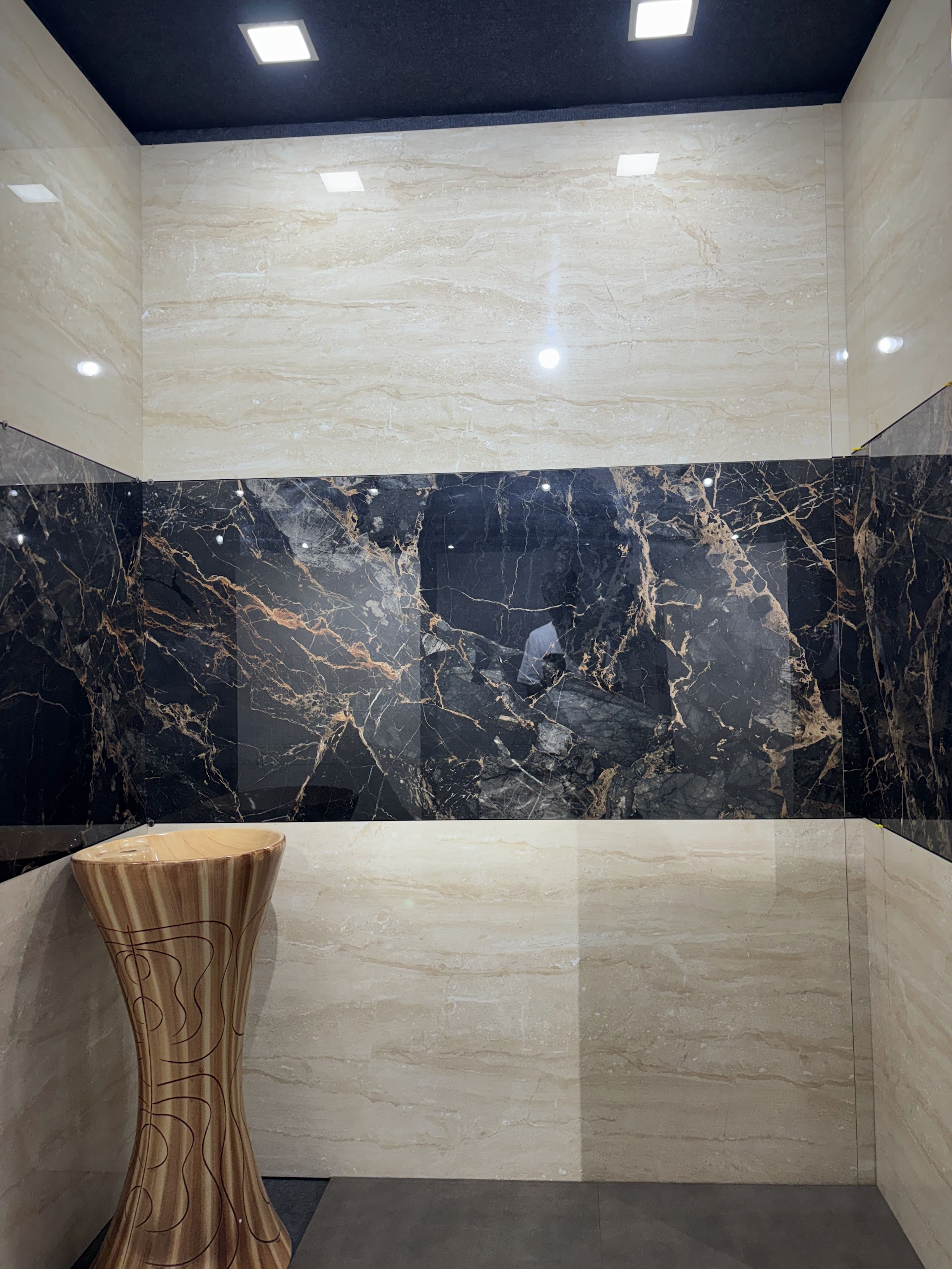 Showroom corner combining pale marble-finish tile panels with a dark veined horizontal band and a sculptural pedestal basin
