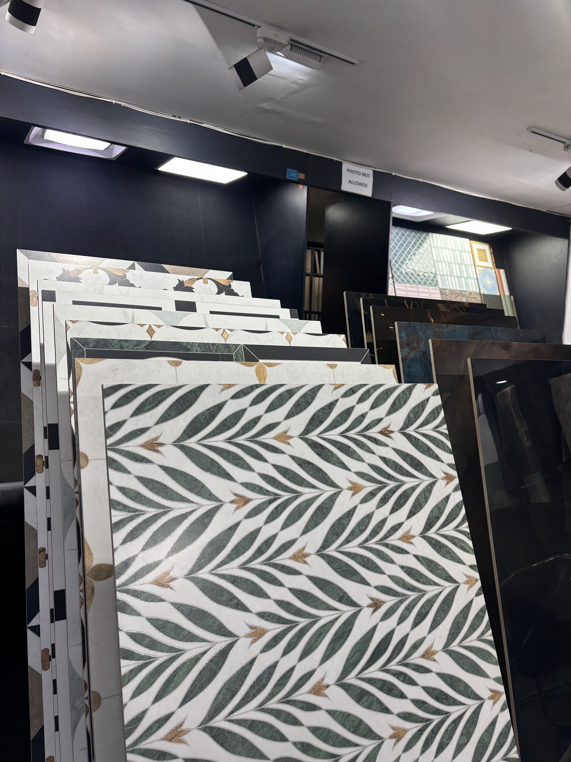 Leaf-pattern tile samples arranged on upright showroom racks beneath ceiling track lights