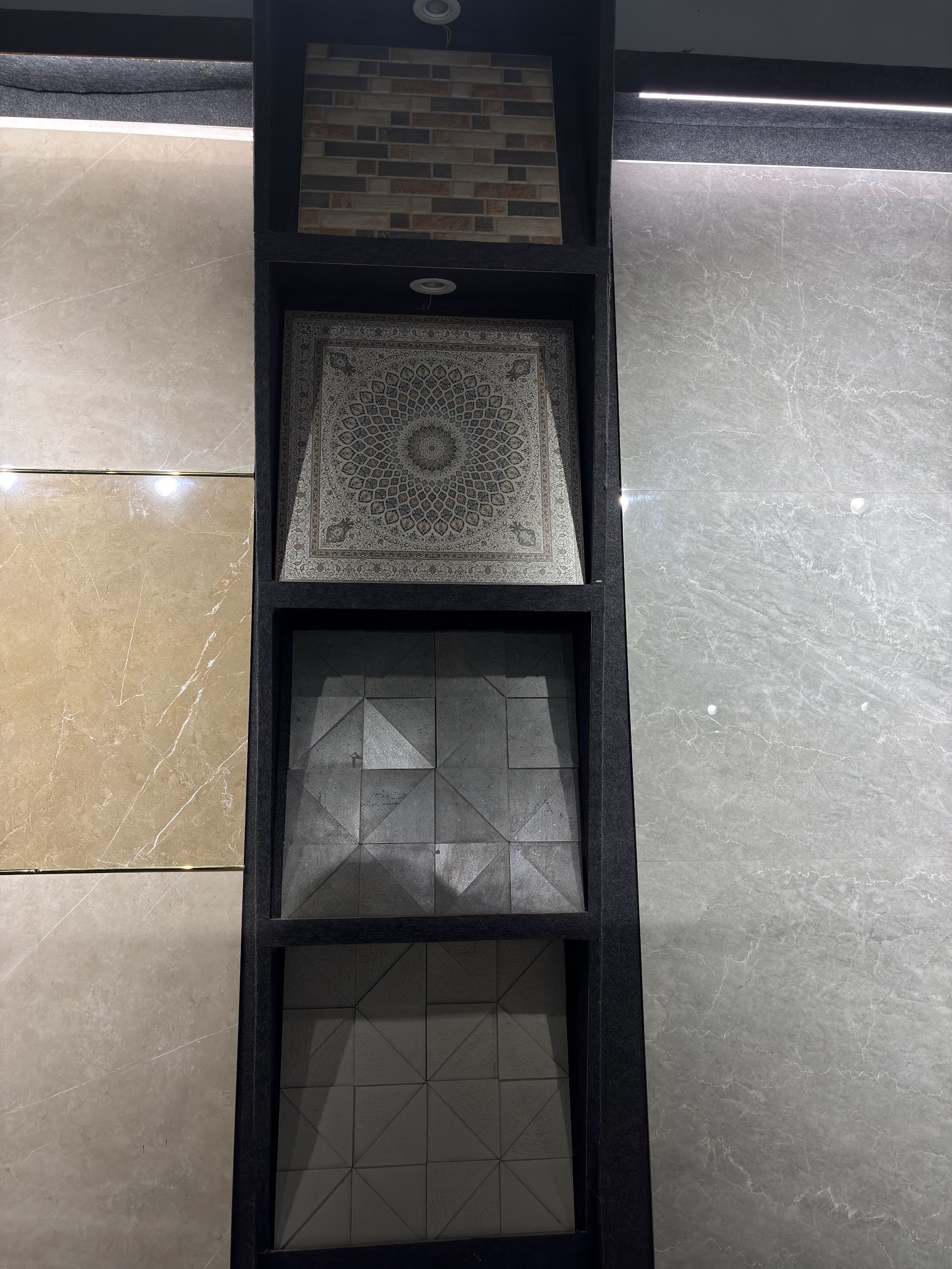 Showroom display of geometric relief tile samples between large neutral marble-finish panels