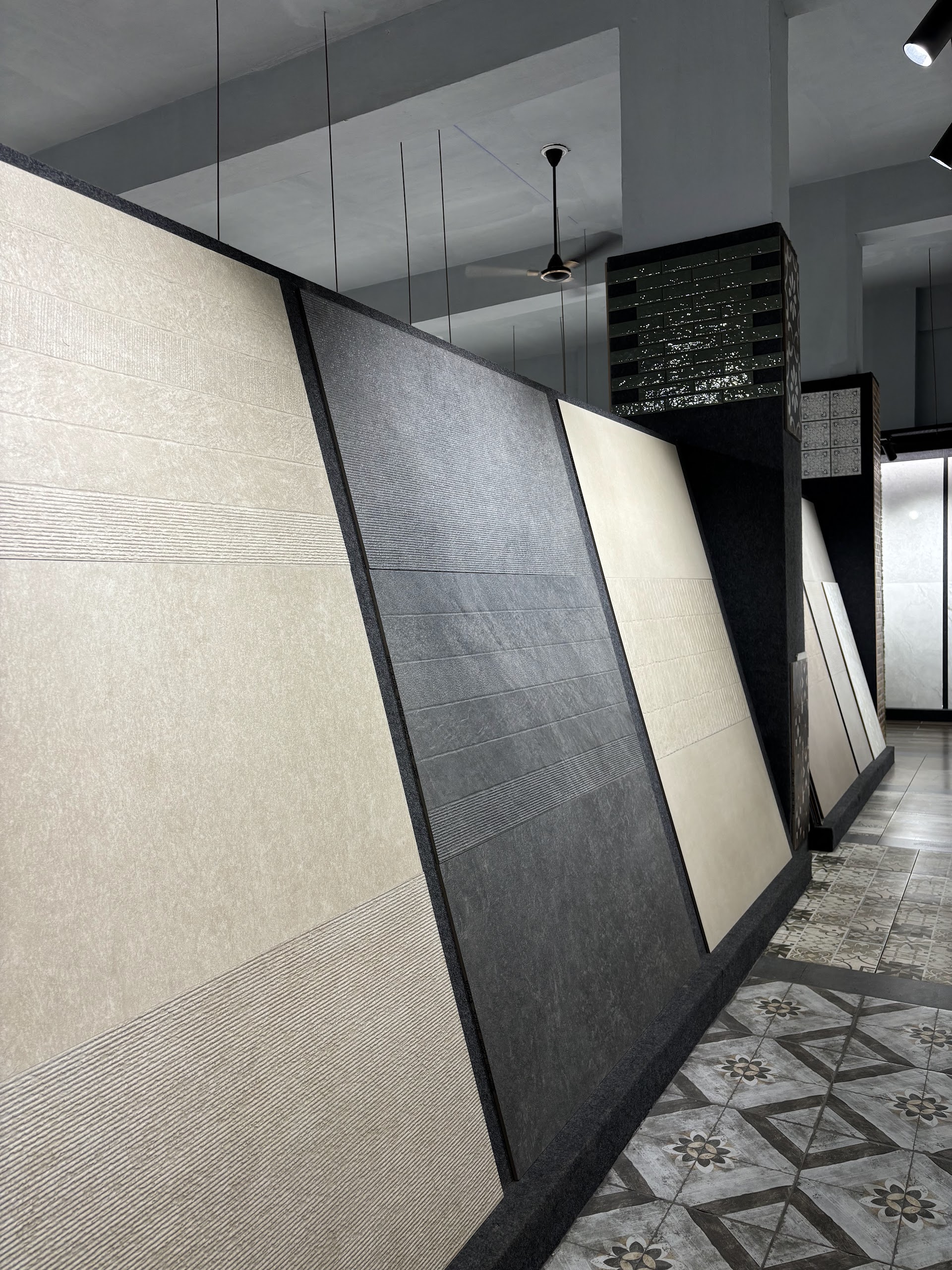 Angled showroom panels displaying pale and grey tile finishes beside a patterned aisle floor