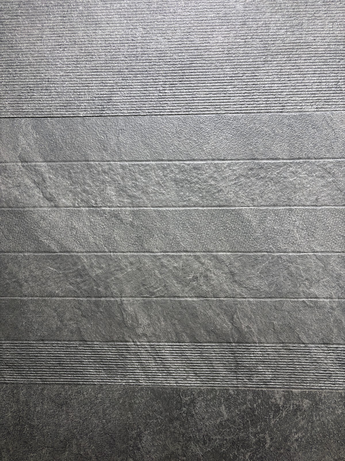 Grey surface samples arranged from fine linear texture to deeper stone finish at World of Tile Noida