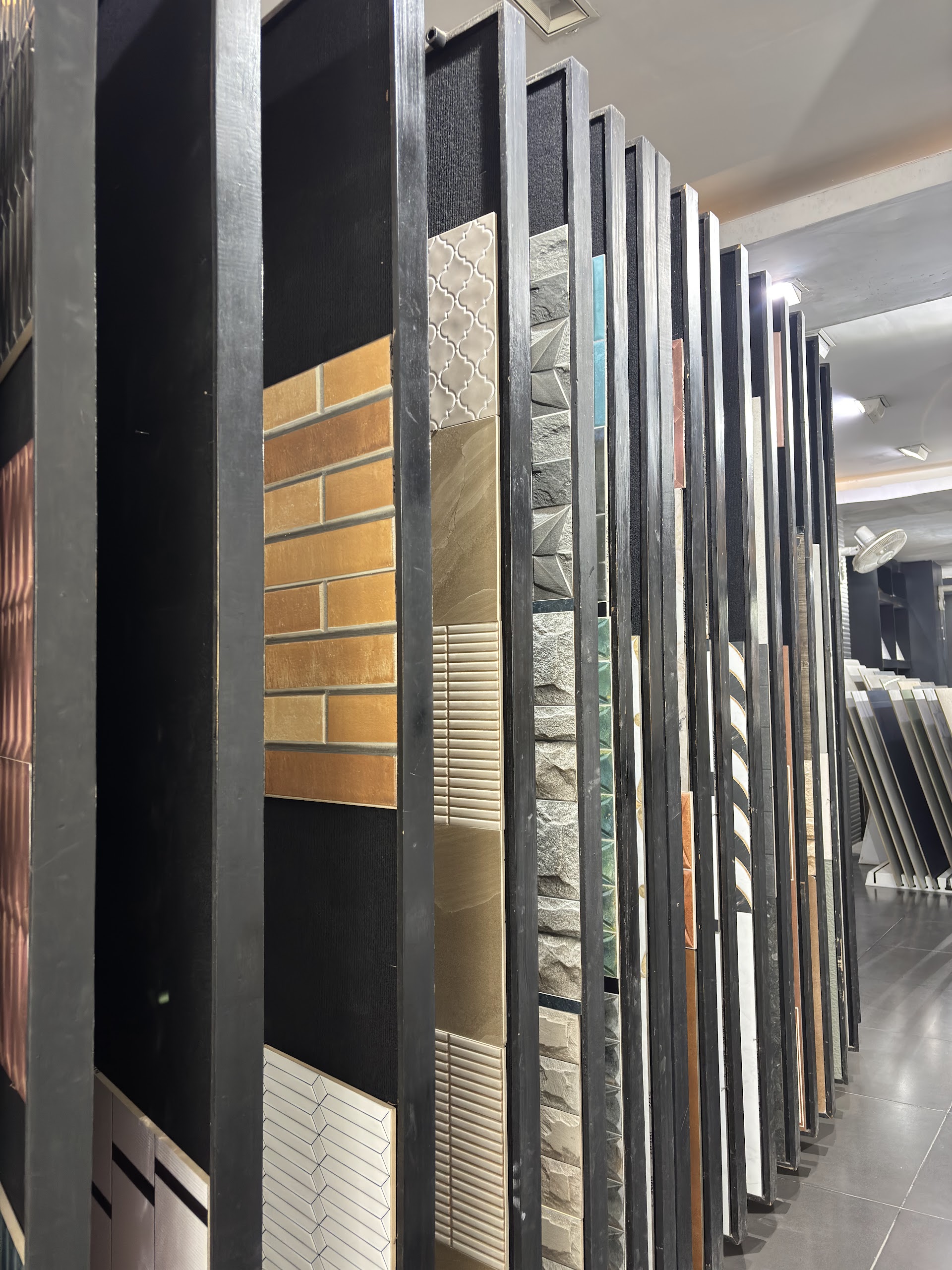 Upright showroom racks containing brick-pattern, textured and neutral tile sample panels