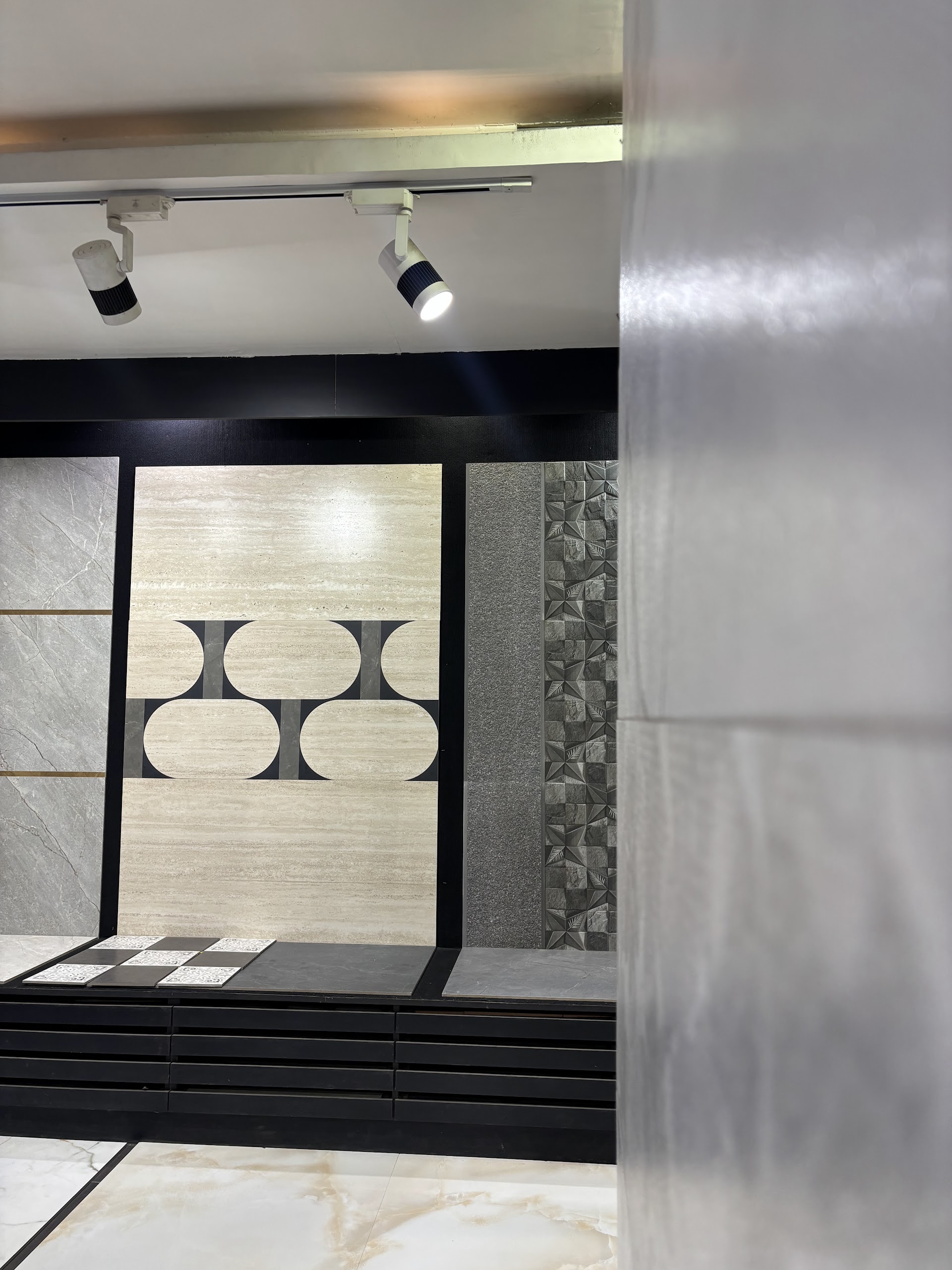 Showroom view with geometric wall panels, ceiling spotlights and a reflective grey tile surface in the foreground